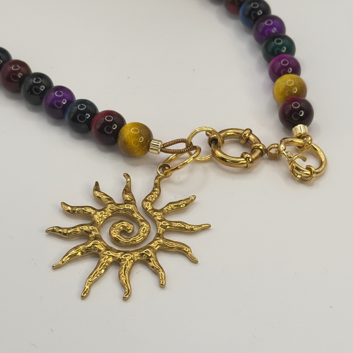 Détail du pendentif soleil doré texturé du collier SOLSTICE™, avec anneaux et perles multicolores.