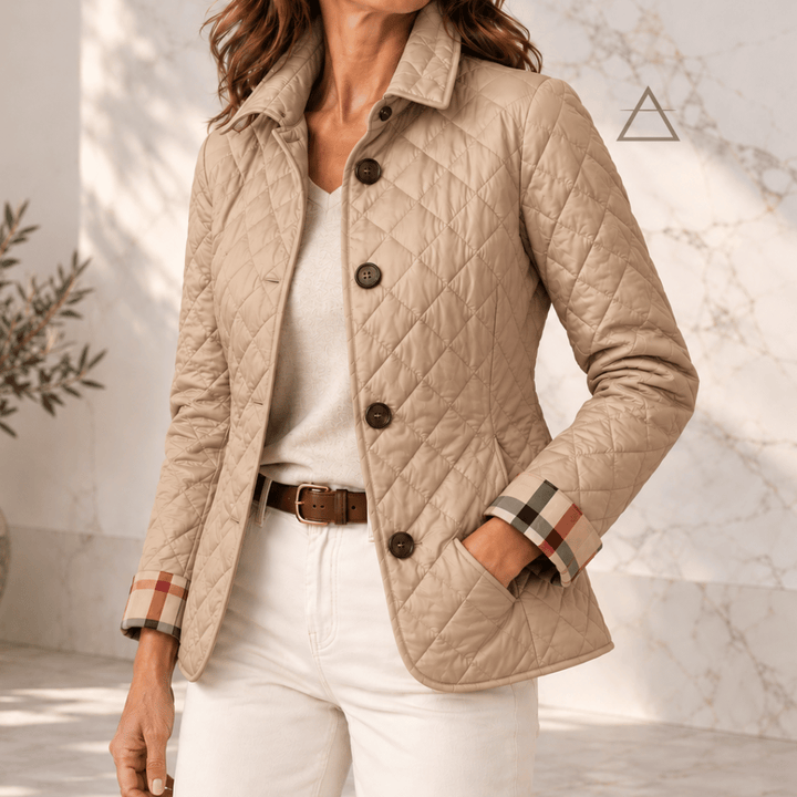 Veste matelassée Margaux en beige sable, portée avec un pantalon écru, avec fermeture boutonnée et revers de poignets à carreaux.
