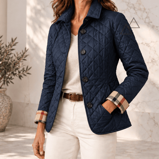 Veste matelassée Margaux en bleu marine, portée avec un pantalon écru, avec fermeture boutonnée et revers de poignets à carreaux.
