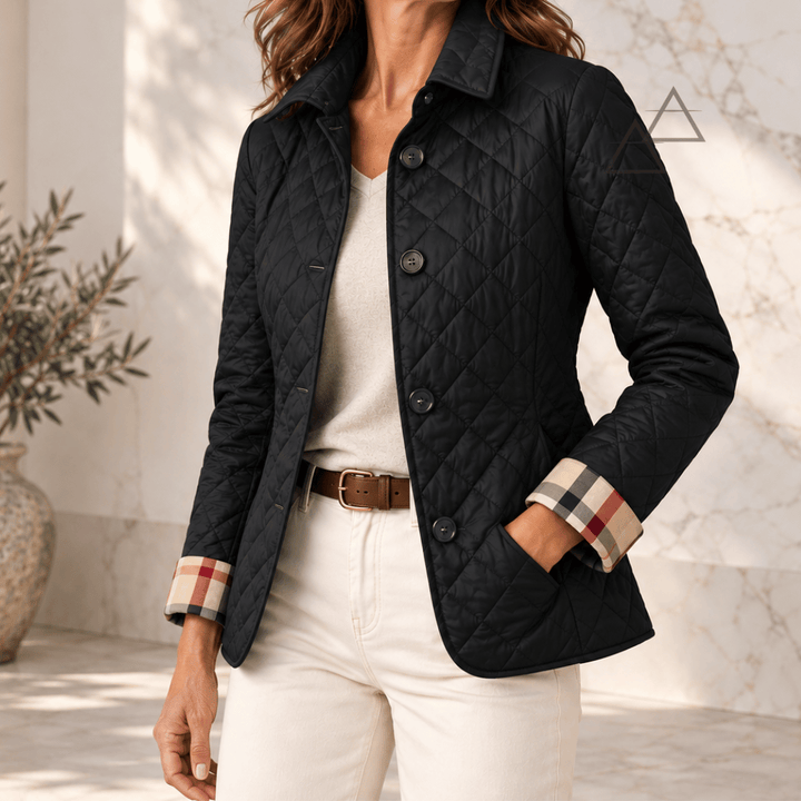 Veste matelassée Margaux en noir, portée avec un pantalon écru, avec fermeture boutonnée et revers de poignets à carreaux.
