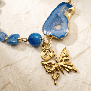 Gros plan sur la tranche d’agate bleue, son centre cristallin et le charm papillon doré de Blue Portal.