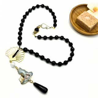 Collier Ocean Midnight en perles noires facettées, avec pendentif bleu pâle, détails dorés et longue goutte noire, présenté à plat.