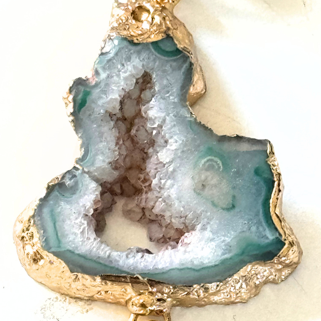 Gros plan sur le cœur cristallin bleu pâle du pendentif Ocean Midnight et sa bordure dorée irrégulière.