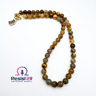 Collier Unspoken disposé en boucle sur fond blanc, avec ses perles aux nuances de brun, de miel et de gris.