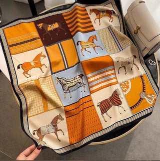 Carré Équestre Orange déployé, à motifs de chevaux et de rayures dans des tons orange, crème, brun et bleu ciel.